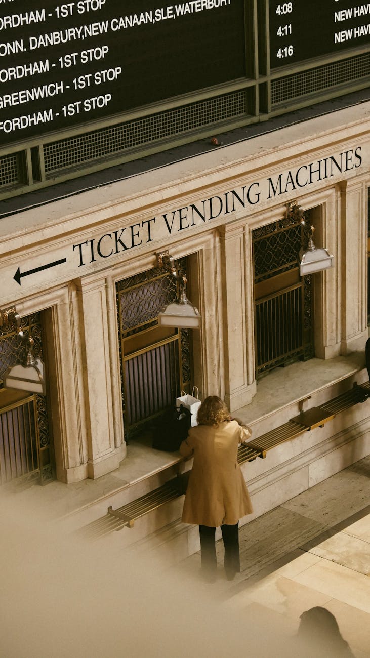 back view shot of a woman in brown trench coat standing near ticket vending machine