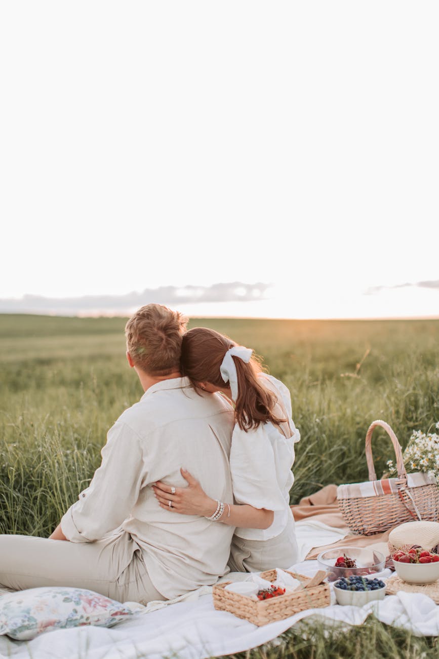 back view shot of a couple sitting on a picnic blanket while looking at the beautiful sky